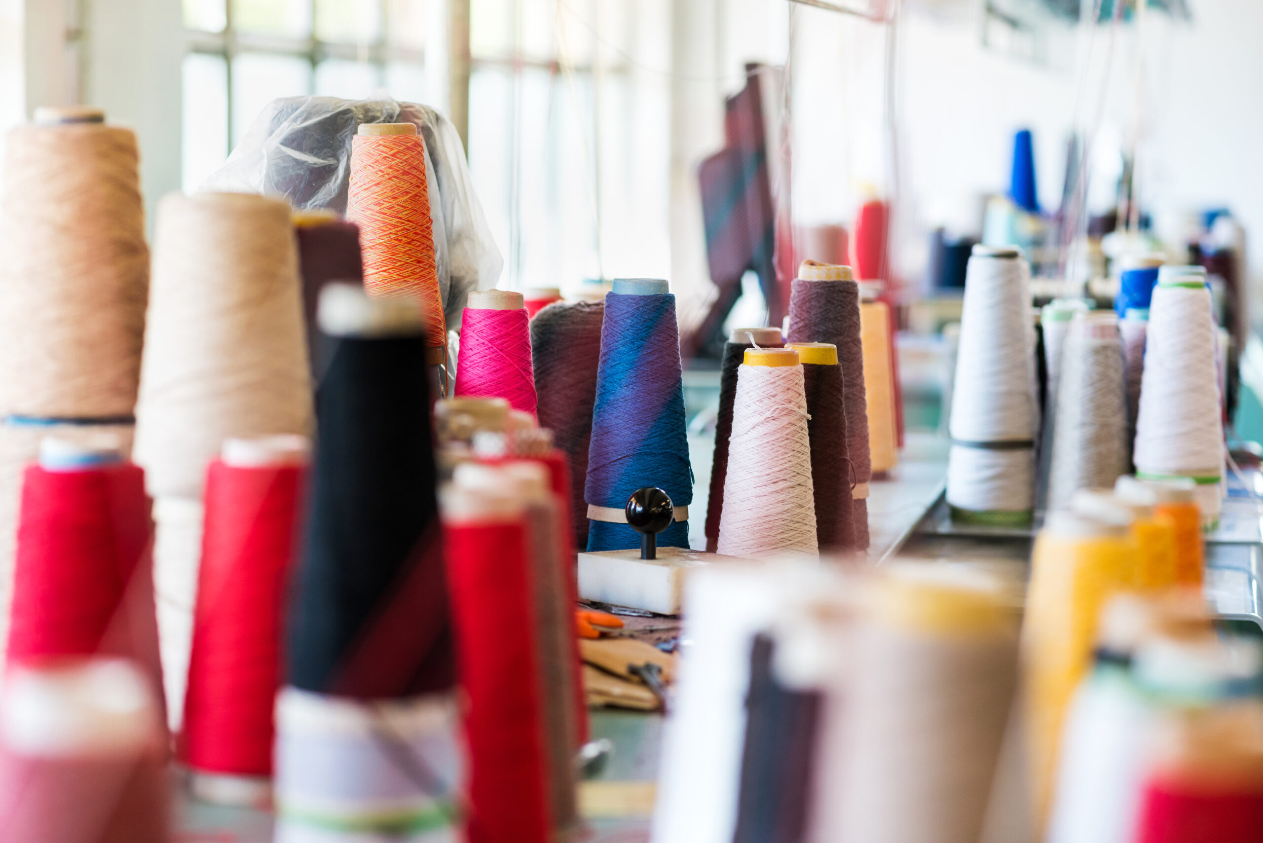 Multiple reels of cashmere wool or yarn in assorted colors on workbenches in a knitwear factory with focus to a stack of spools on a table in the center